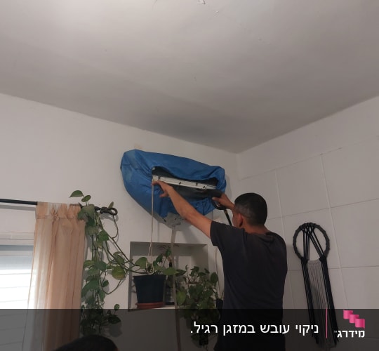 אדם מנקה מזגן עם כיסוי כחול על הקיר